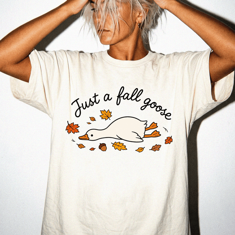 A person wearing a white t-shirt with a graphic design of a duck surrounded by autumn leaves.