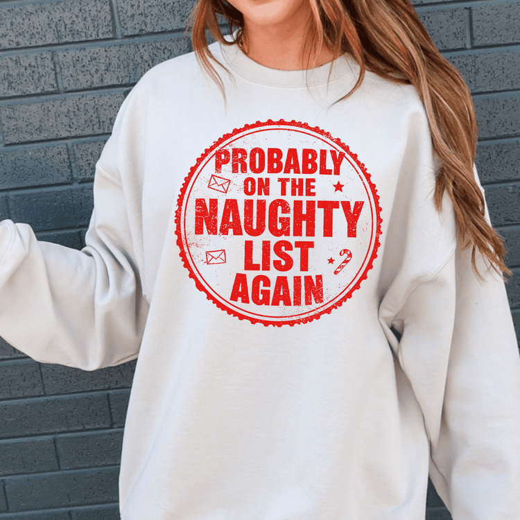 A white sweatshirt with a red circular design that says "Probably on the Naughty List Again" printed on it.