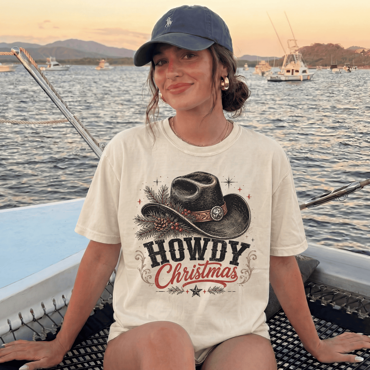 A woman wearing a hat and a t-shirt with a cowboy hat and the text "HOWDY CHRISTMAS" is sitting on a boat in the water.