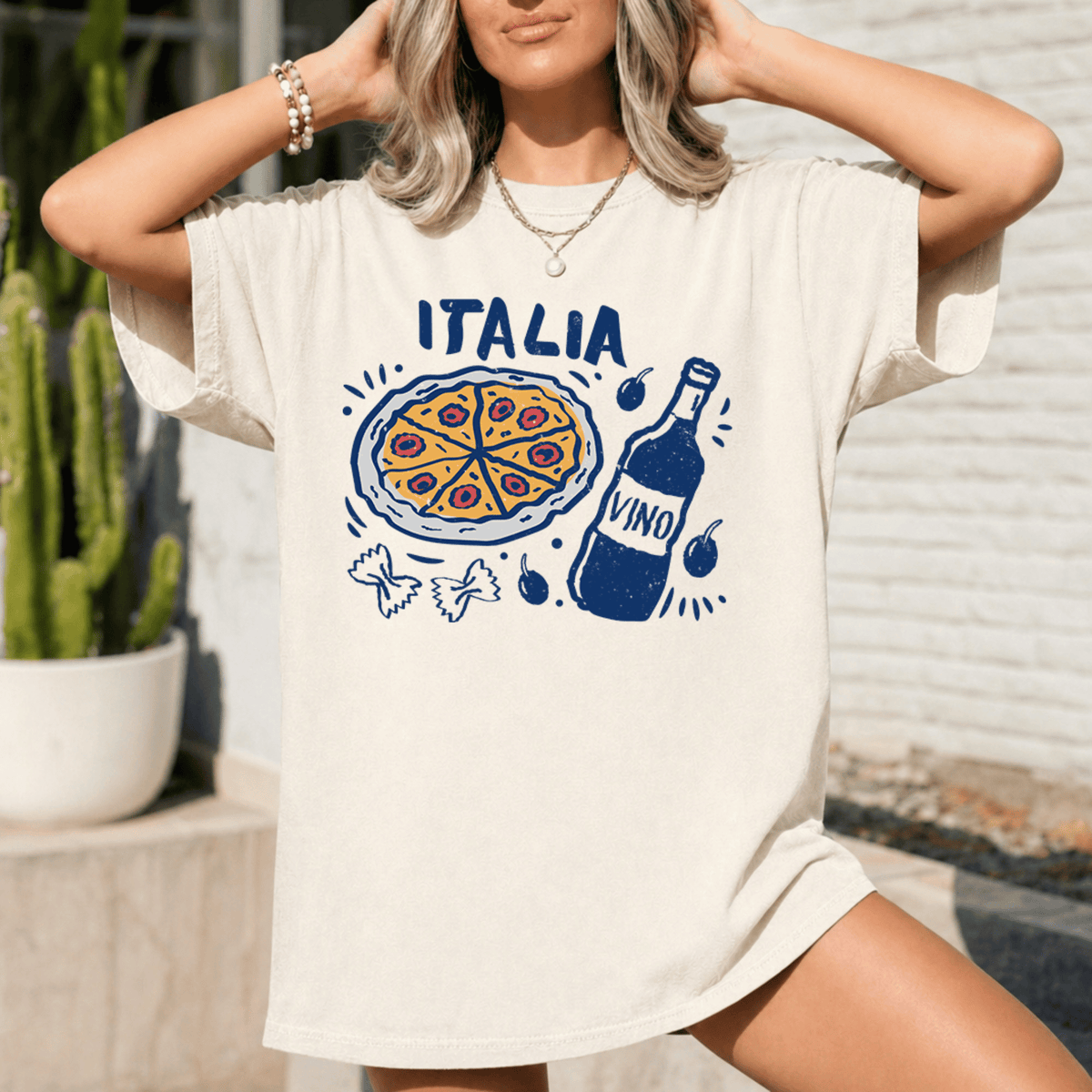 A woman wearing a white t-shirt with a graphic design of a pizza and wine bottle, along with other Italian-themed elements.