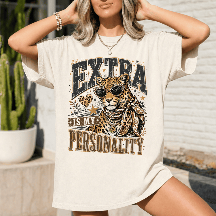 A woman wearing a white t-shirt with a graphic design of a leopard and the text "EXTRA IS MY PERSONALITY" printed on it.