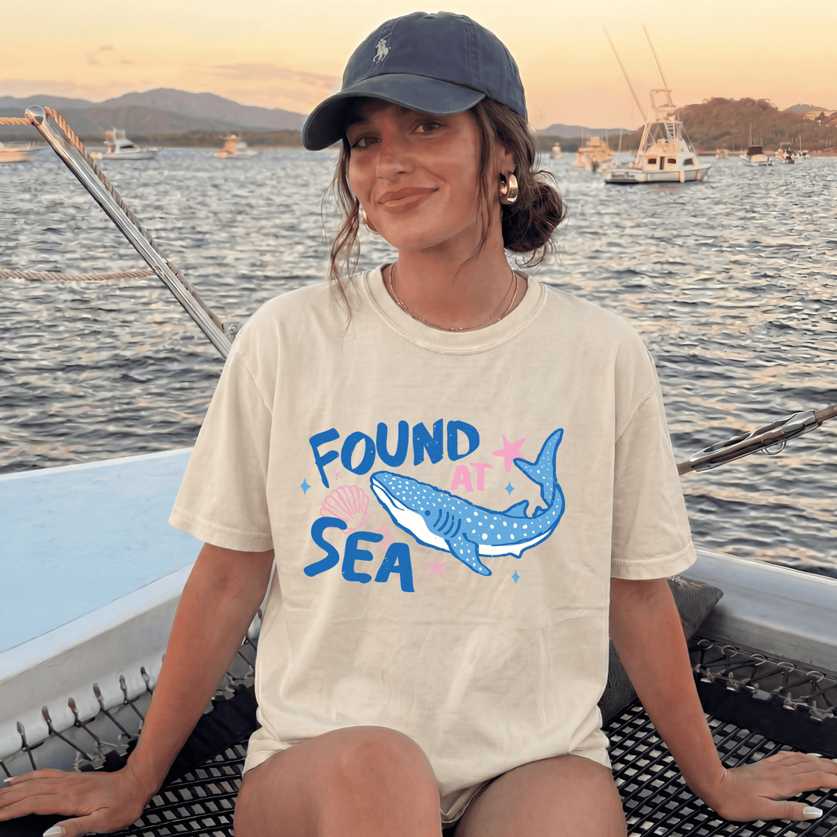 A woman wearing a white t-shirt with a graphic of a whale and the text "FOUND SEA" is sitting on a boat in the ocean.