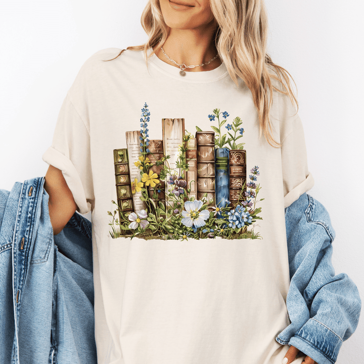 A woman wearing a white t-shirt with a printed design of books surrounded by flowers and plants.