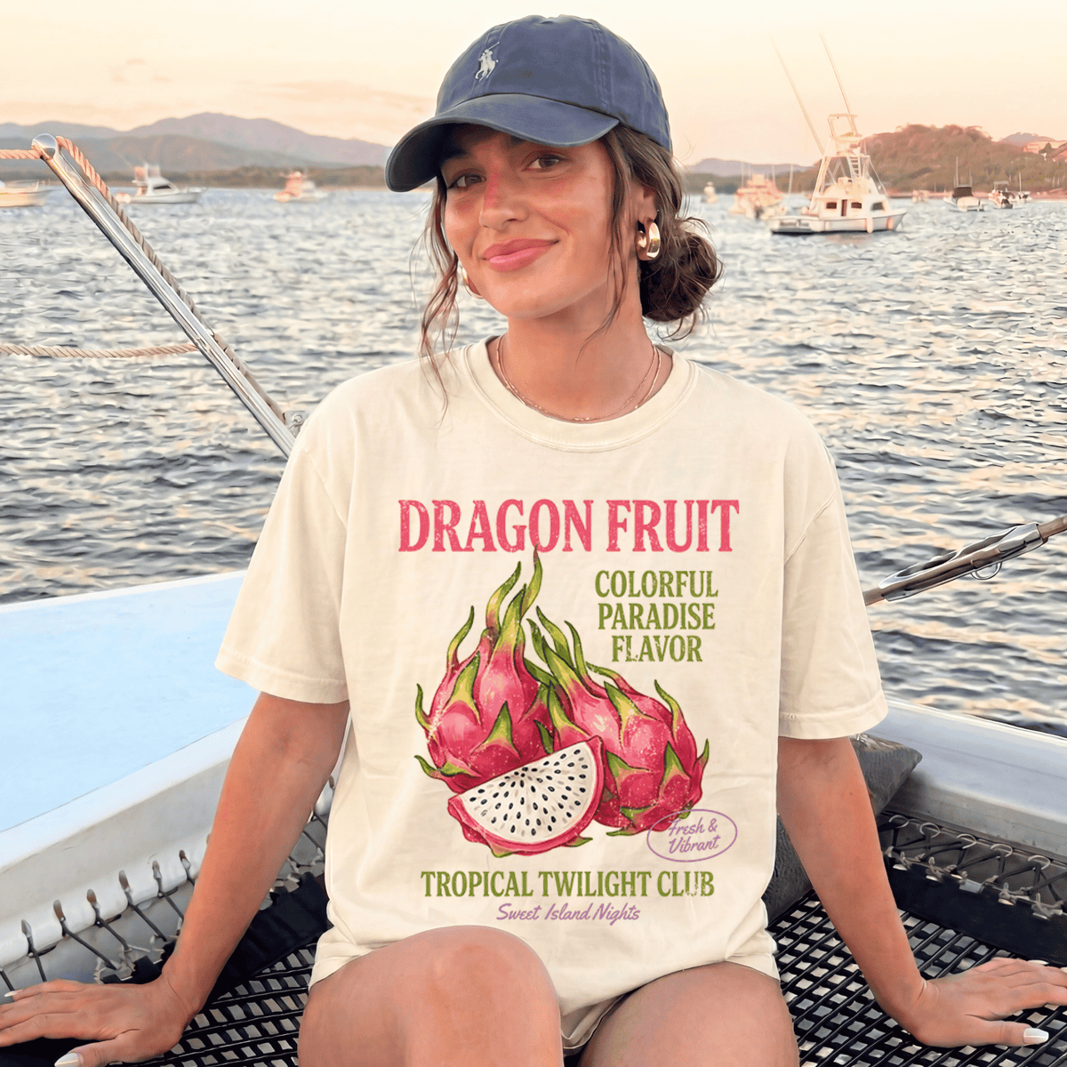 A woman wearing a white t-shirt with a dragon fruit graphic and text, sitting on a boat in the water.