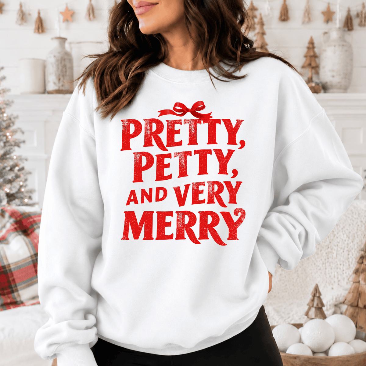 A woman wearing a white sweatshirt with the text "PRETTY, PETTY, AND VERY MERRY" printed on it.