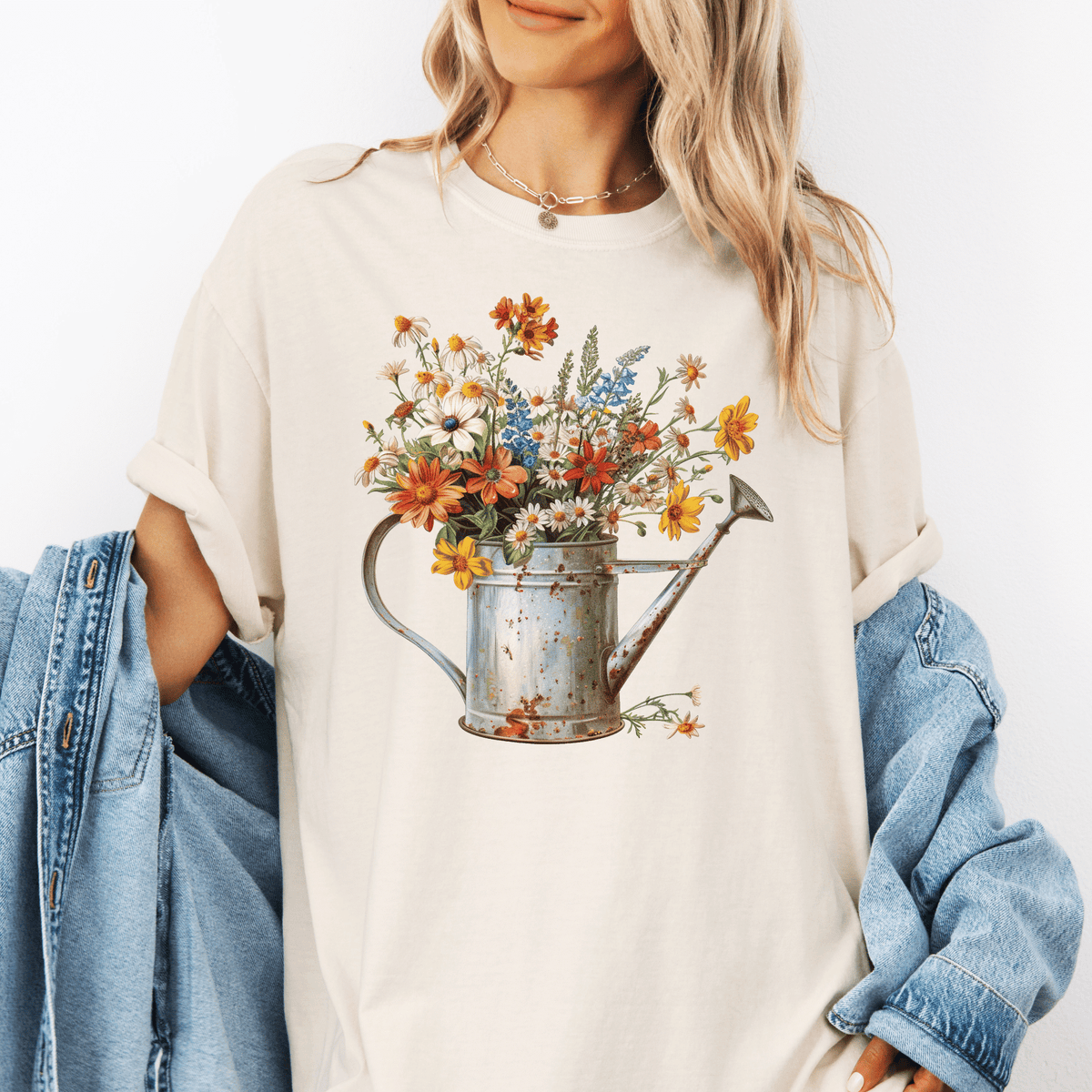 A woman wearing a white t-shirt with a printed image of a watering can filled with colorful flowers.