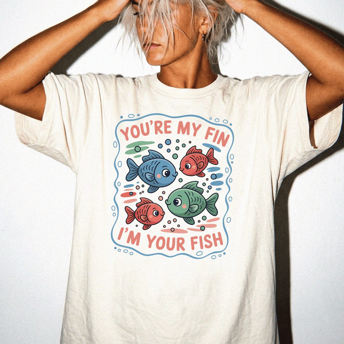 A person wearing a white t-shirt with a graphic design featuring colorful fish and the text "You're my fin, I'm your fish".