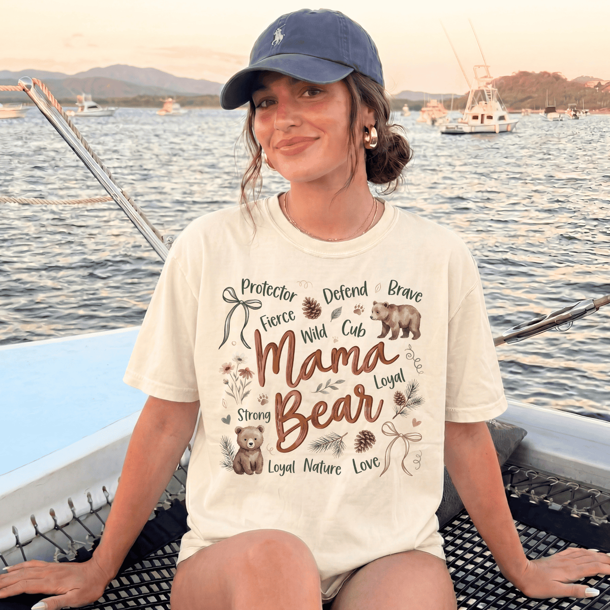 A woman wearing a white t-shirt with a graphic design and text, sitting on a boat in the water with mountains in the background.
