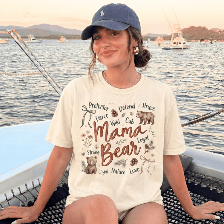 A woman wearing a white t-shirt with a graphic design and text, sitting on a boat in the water with mountains in the background.