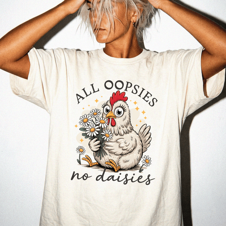 A person wearing a white t-shirt with a graphic design of a chicken holding flowers and the text "All Oopsies no daisies" printed on it.