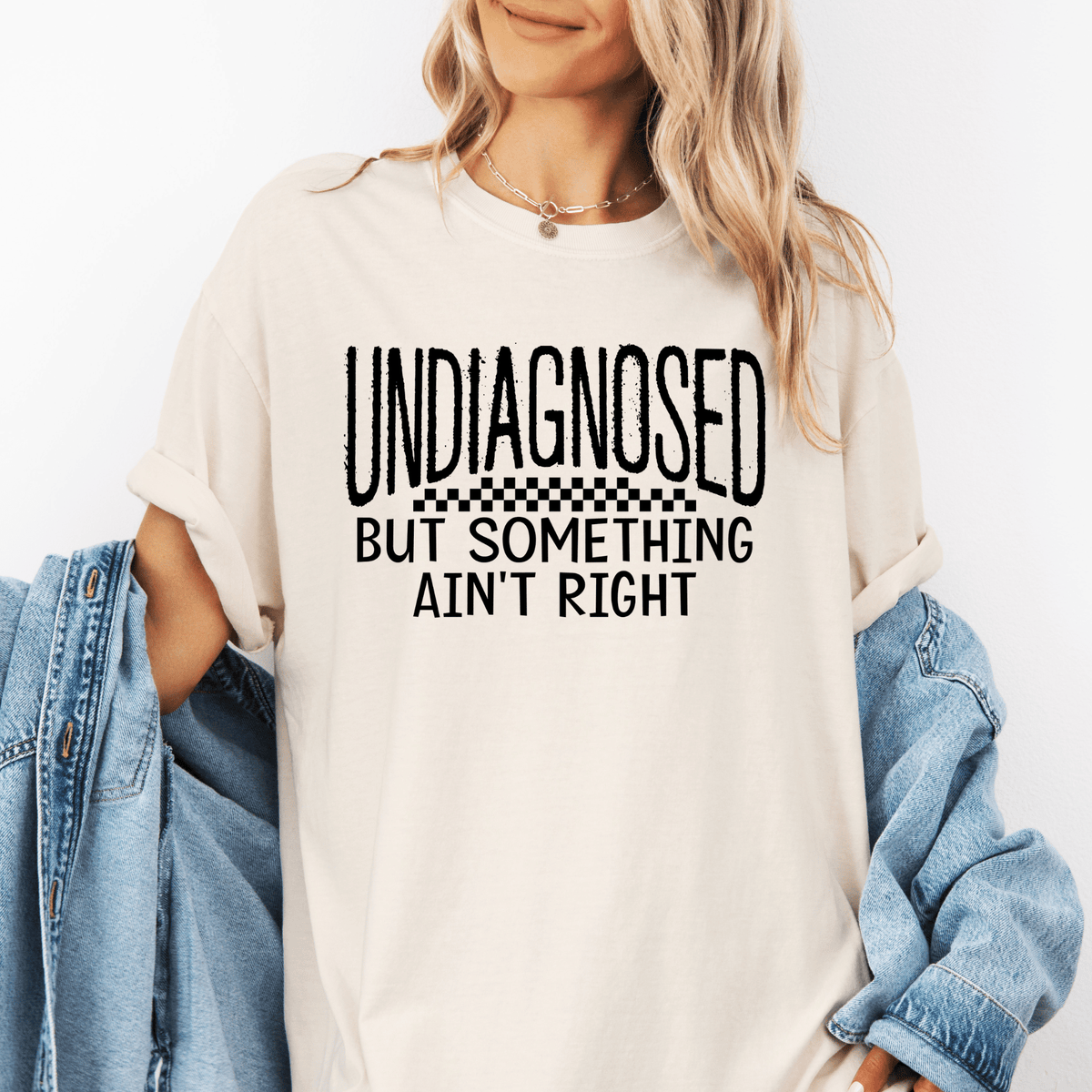 A woman wearing a white t-shirt with the text "UNDIAGNOSED BUT SOMETHING AIN'T RIGHT" printed on it.