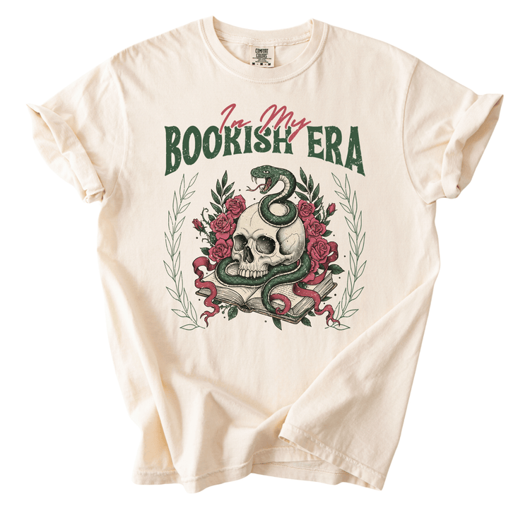 A white t-shirt with a graphic design featuring a skull, a snake, and flowers, along with the text "I'm my BOOKISH ERA" printed on it.