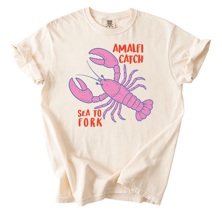 a white t-shirt with a graphic design of a pink lobster and the text "Amalfi Catch Sea to Fork" printed on it.