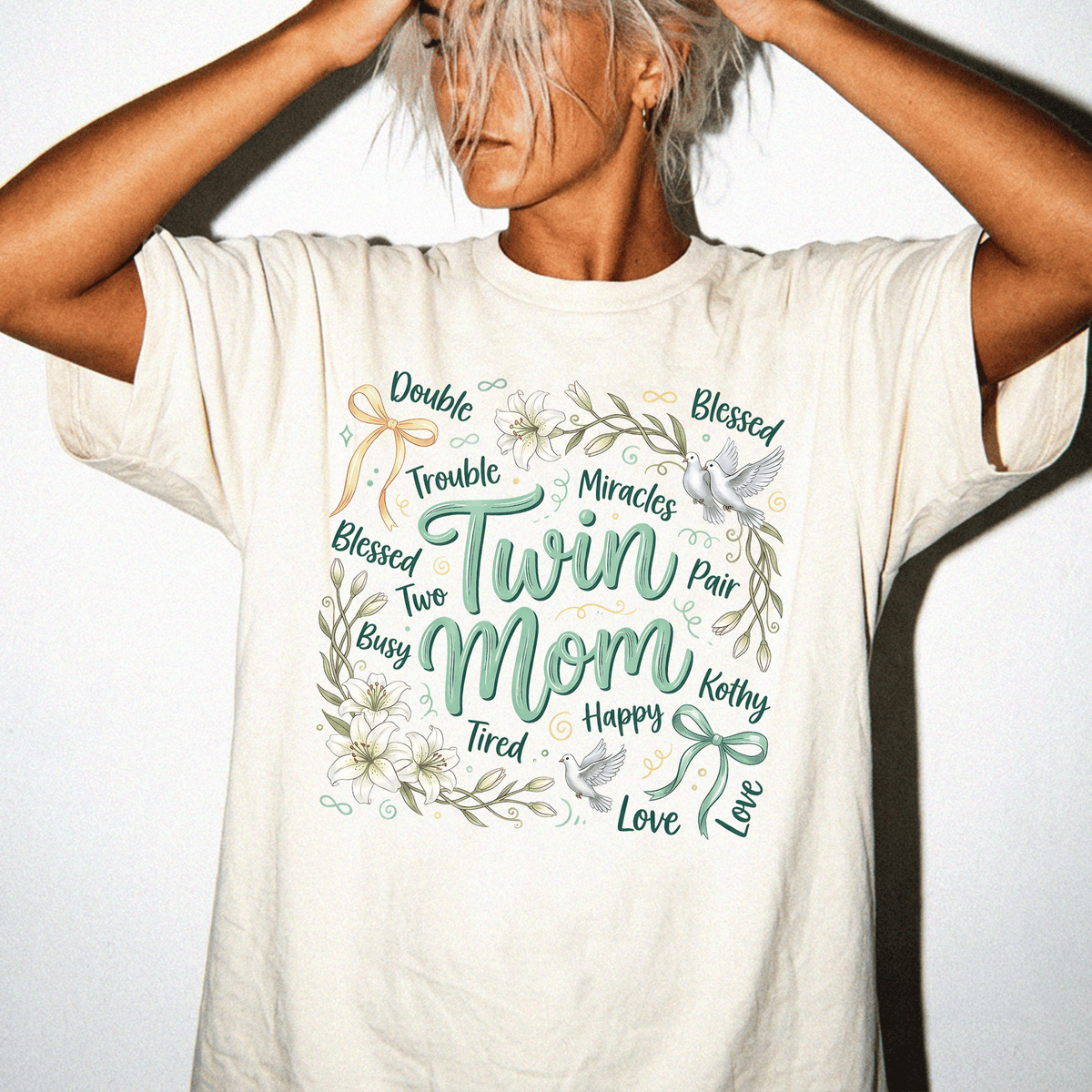 A woman wearing a white t-shirt with a graphic design featuring the words "Twin Mom" surrounded by floral elements.