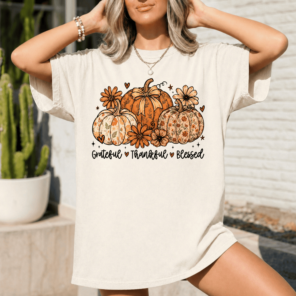 A woman wearing a white t-shirt with a graphic design of pumpkins and flowers, along with the text "Gratitude, Thankful, Blessed".