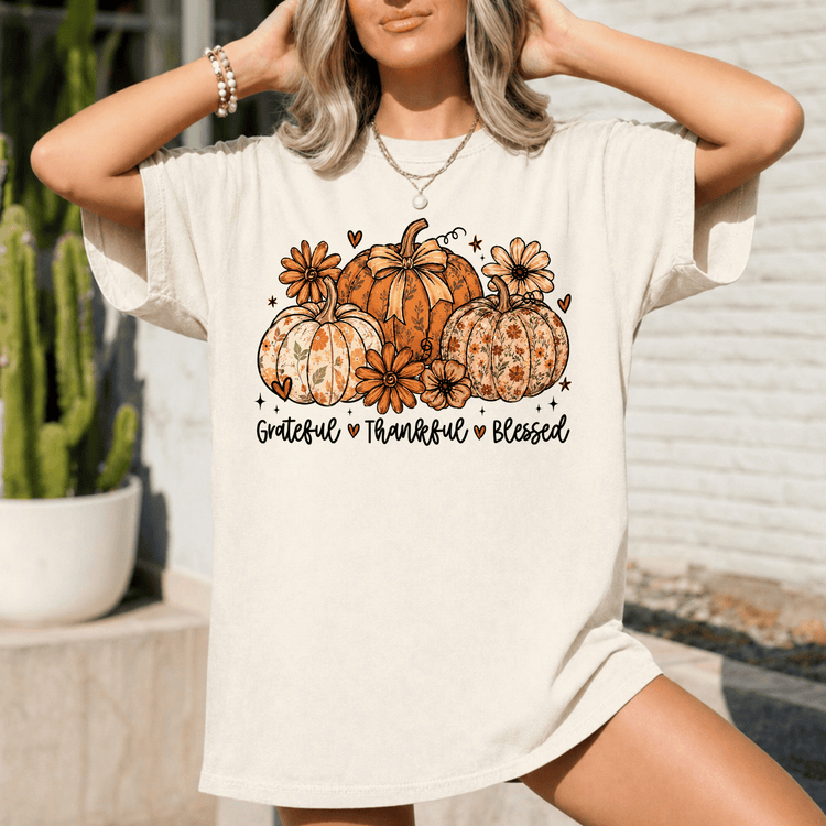 A woman wearing a white t-shirt with a graphic design of pumpkins and flowers, along with the text "Gratitude, Thankful, Blessed".