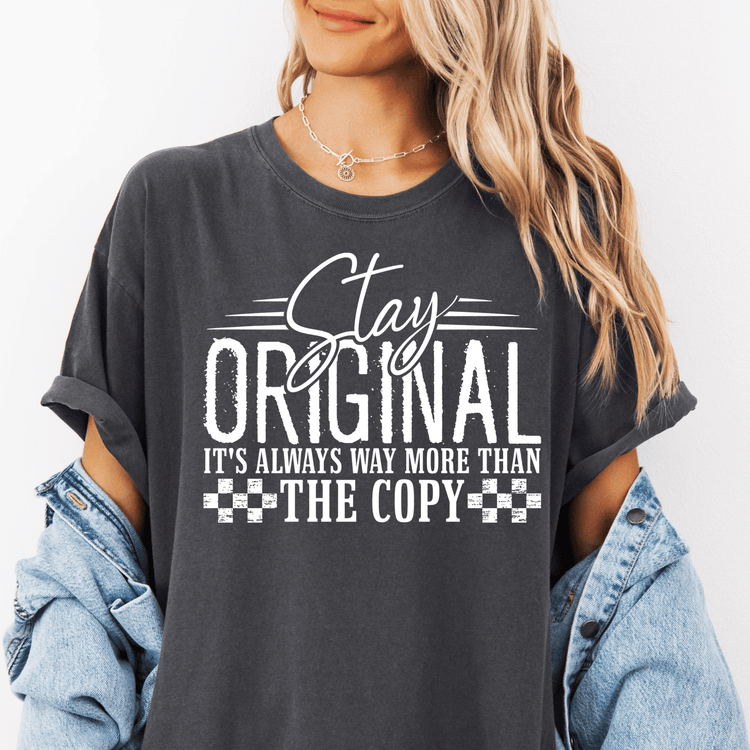 A woman wearing a gray t-shirt with the text "Stay Original It's Always Way More Than The Copy" printed on it.