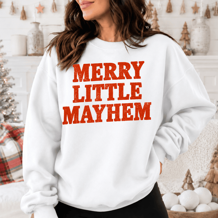 A woman wearing a white sweatshirt with the text "MERRY LITTLE MAYHEM" printed on it.