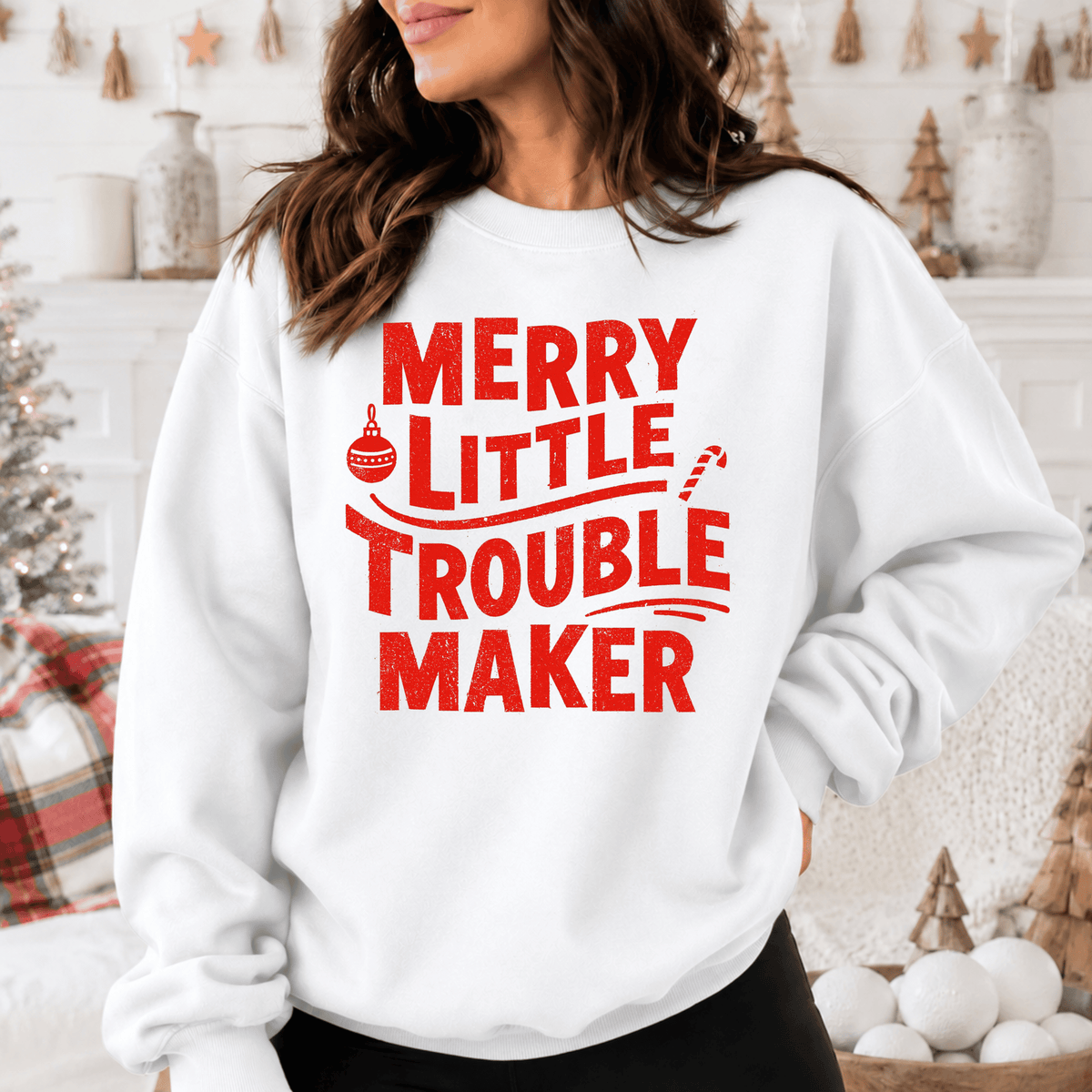 A woman wearing a white sweatshirt with the text "MERRY LITTLE TROUBLE MAKER" printed on it.
