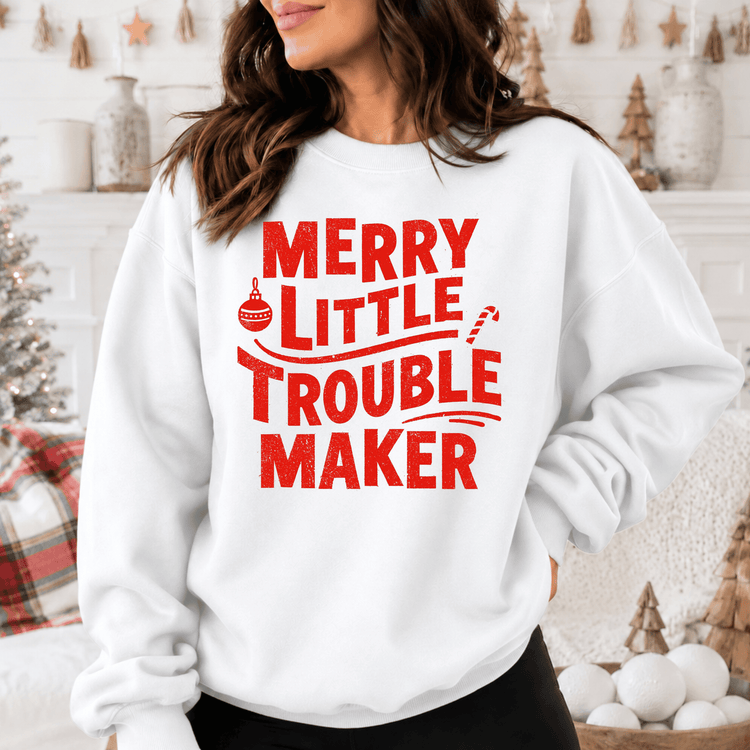 A woman wearing a white sweatshirt with the text "MERRY LITTLE TROUBLE MAKER" printed on it.
