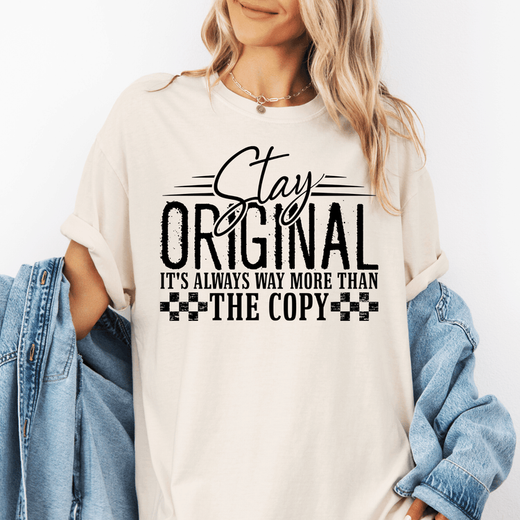 A woman wearing a white t-shirt with the text "Stay original it's always way more than the copy" printed on it.