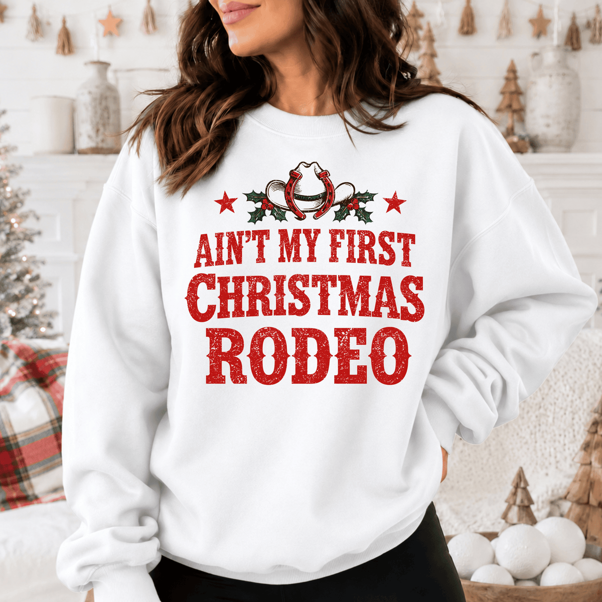 A woman wearing a white sweatshirt with a red and white graphic design that says "Ain't My First Christmas Rodeo".