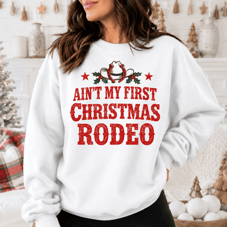 A woman wearing a white sweatshirt with a red and white graphic design that says "Ain't My First Christmas Rodeo".
