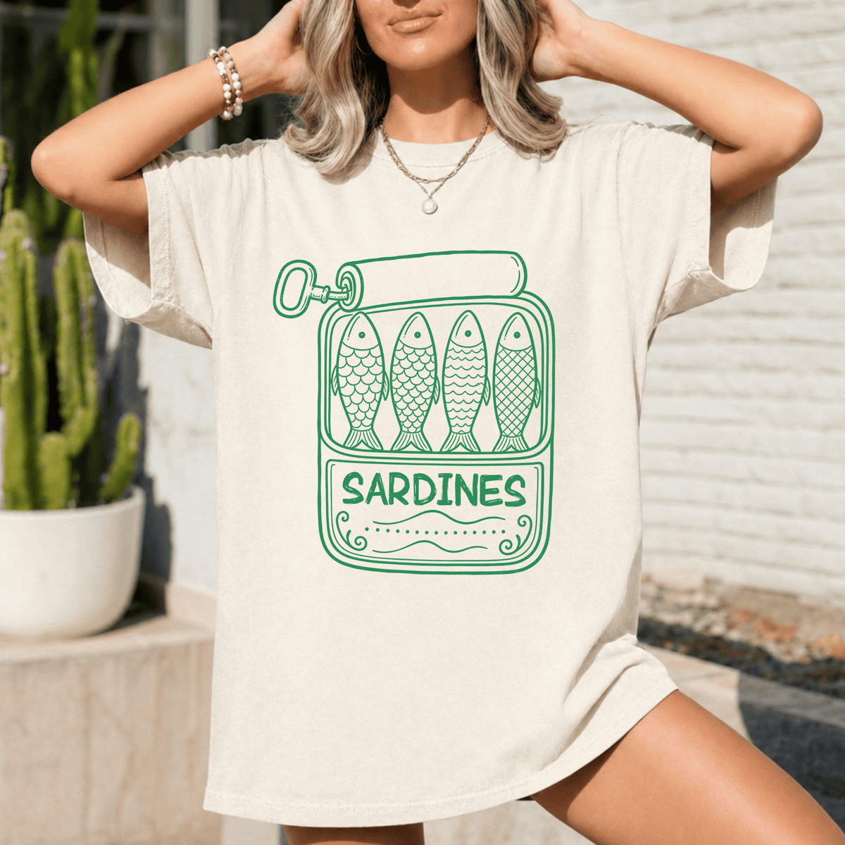A woman wearing a white t-shirt with a graphic design of four fish in a can, along with the text "Sardines" printed on it.