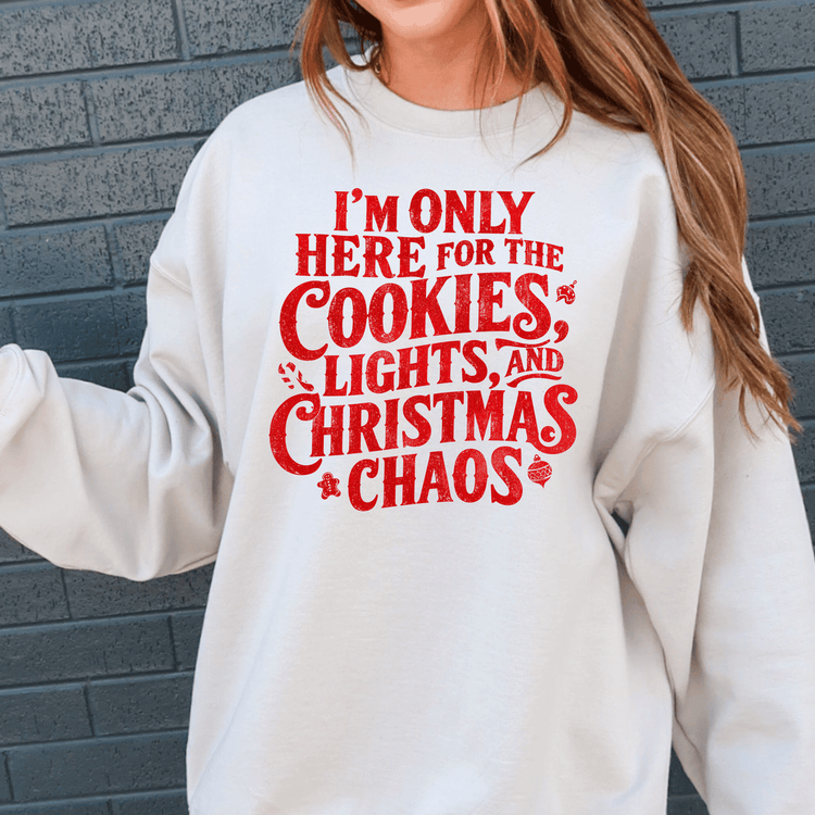 A white sweatshirt with a red text design that reads "I'M ONLY HERE FOR THE COOKIES, LIGHTS, AND CHRISTMAS CHAOS".