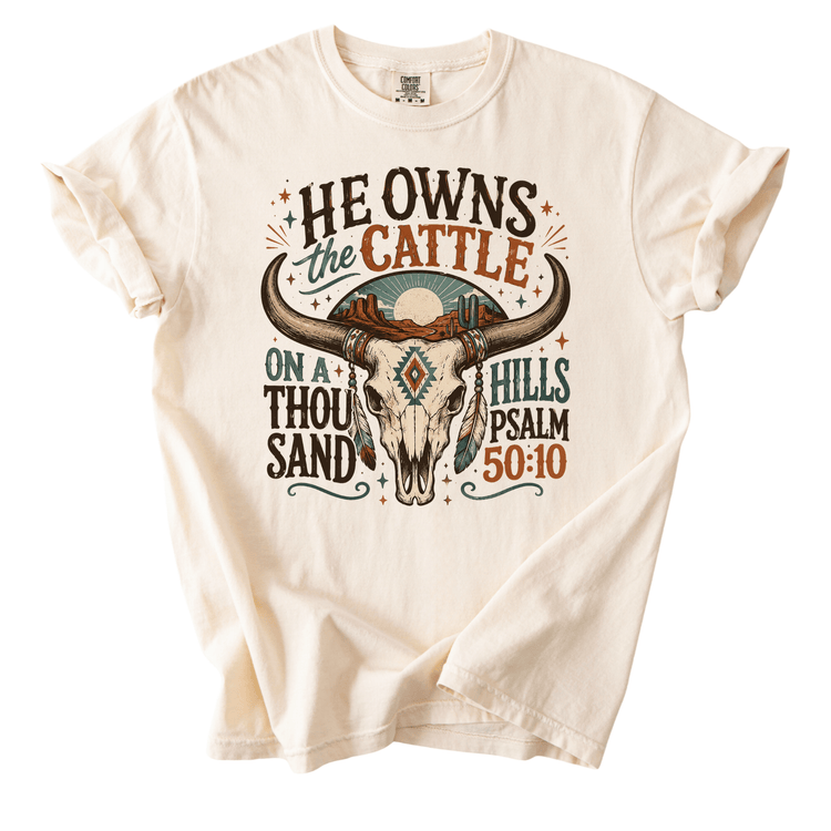 A white t-shirt with a graphic design featuring a bull's head and text that reads "He owns the cattle on a thousand sand".