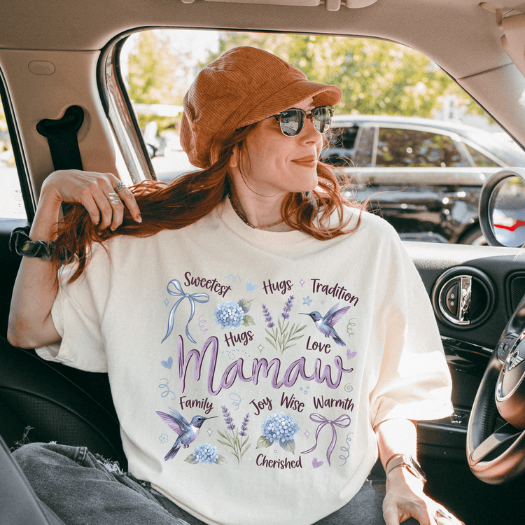 A woman wearing a white t-shirt with a graphic design and text, sitting in a car with a hat on her head.