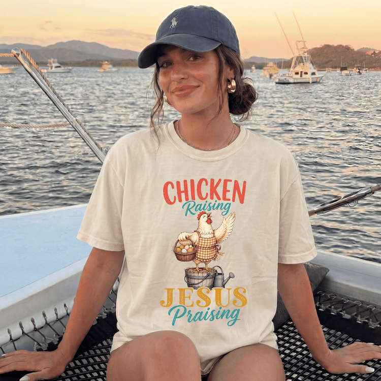 A woman wearing a baseball cap and a t-shirt with a chicken graphic is sitting on a boat, smiling at the camera.