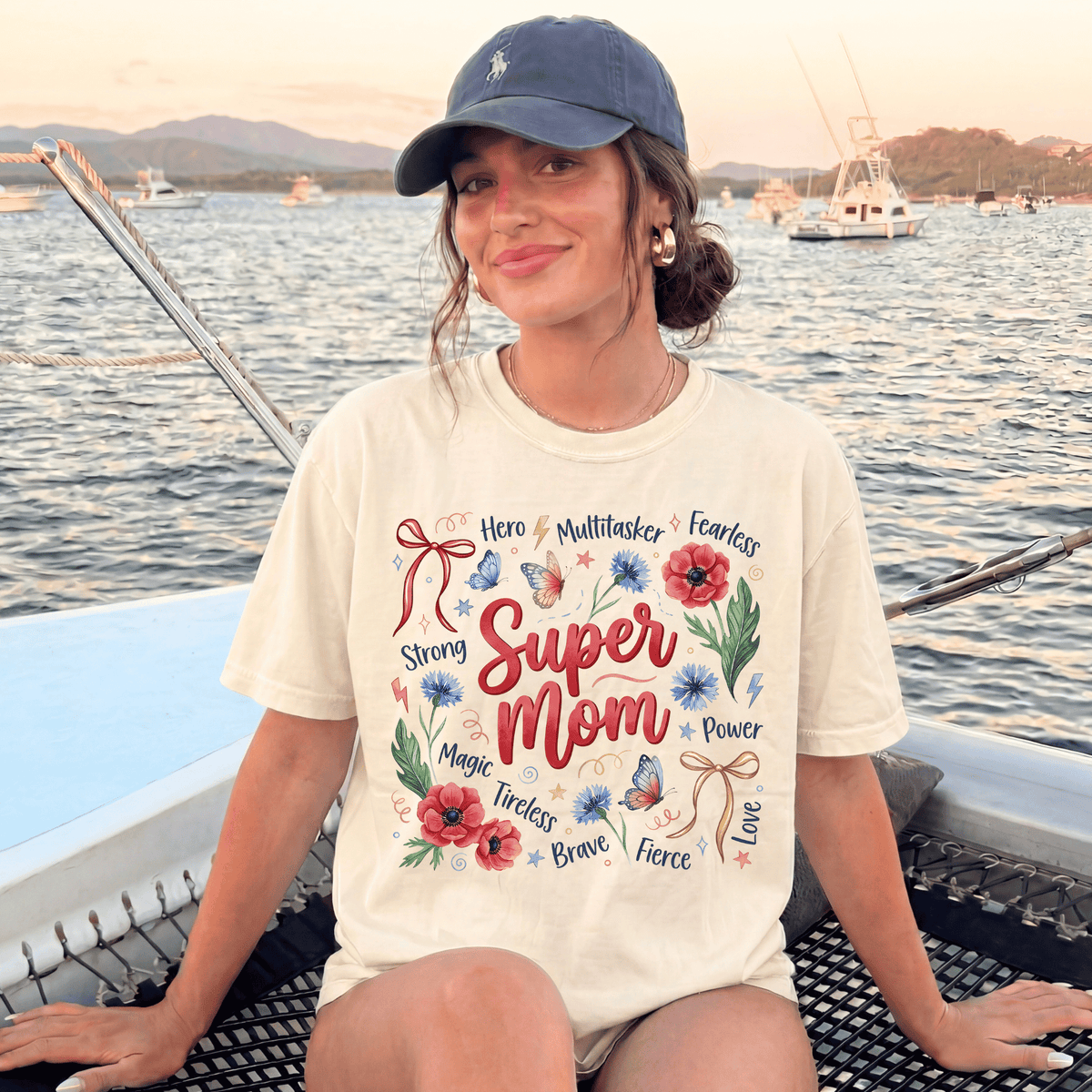 A woman wearing a white t-shirt with a graphic design and text, sitting on a boat in the water with mountains in the background.