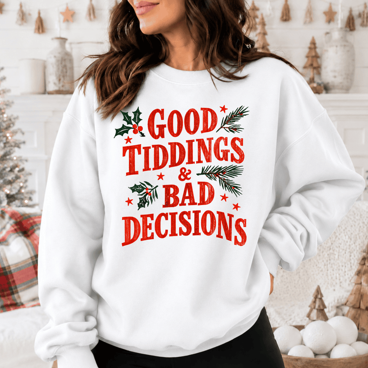 A woman wearing a white sweatshirt with the text "GOOD TIDDINGS & BAD DECISIONS" printed on it.