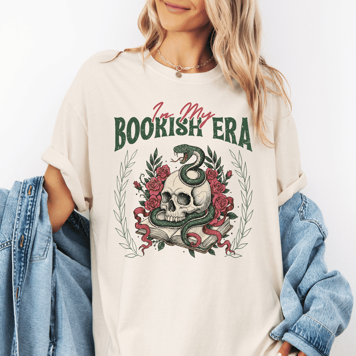 A woman wearing a white t-shirt with a graphic design of a skull and a snake wrapped around it, surrounded by flowers and leaves.