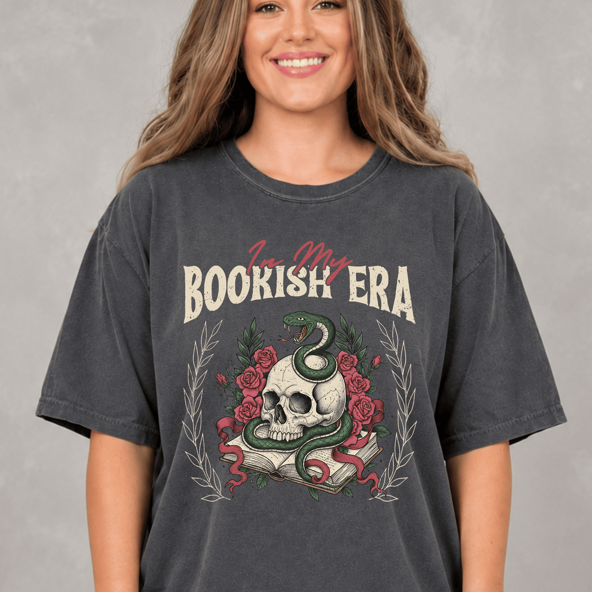 A woman wearing a gray t-shirt with a graphic design featuring a skull, a snake, and a book.