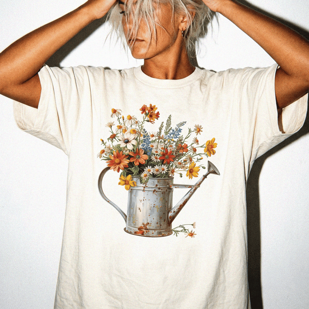 A person wearing a white t-shirt with a printed image of a watering can filled with colorful flowers.
