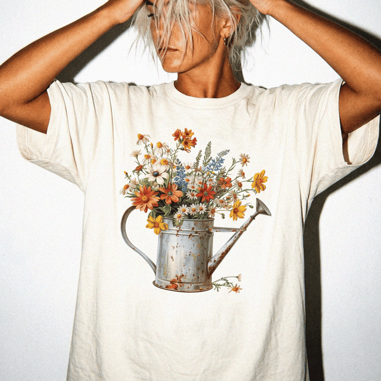 A person wearing a white t-shirt with a printed image of a watering can filled with colorful flowers.
