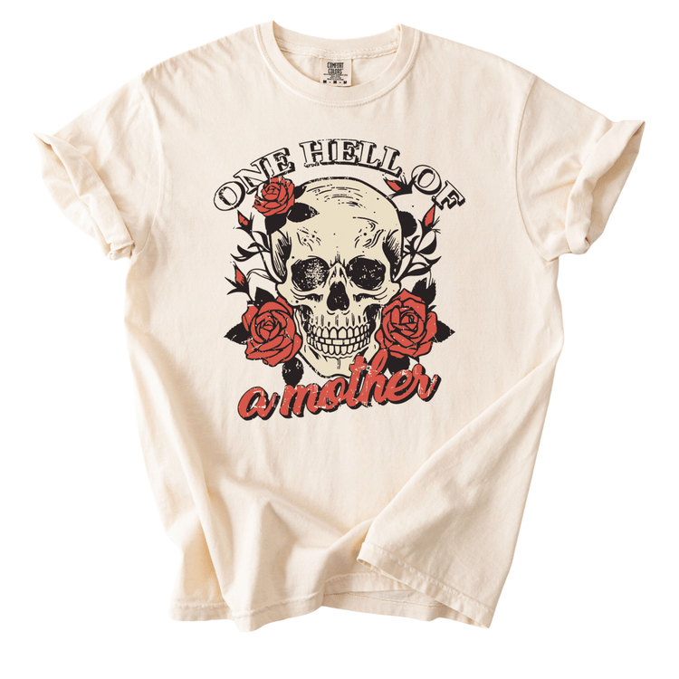 A white t-shirt with a graphic design featuring a skull and roses, along with the text "One Hell of a Mother".