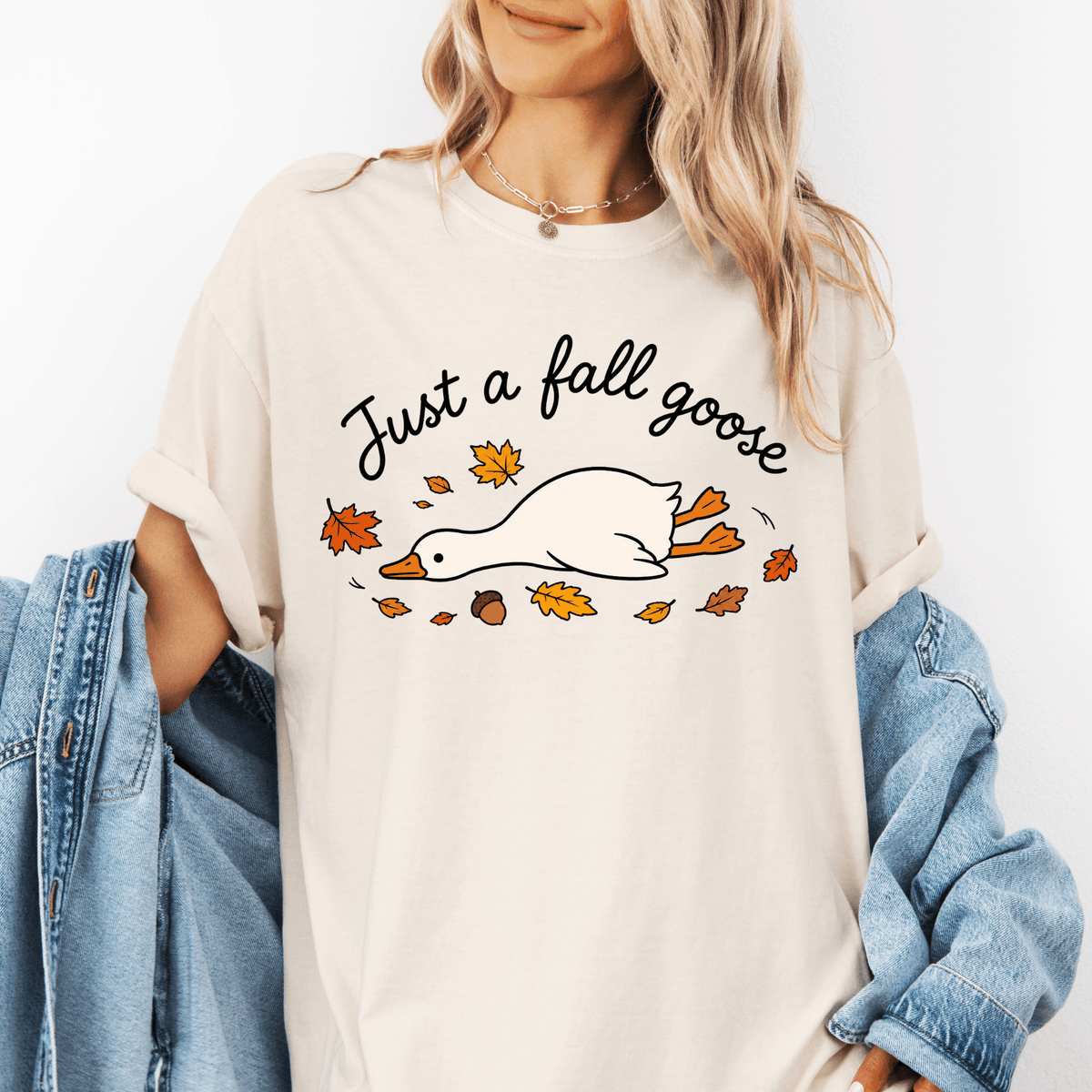A woman wearing a white t-shirt with a graphic design of a goose surrounded by autumn leaves.