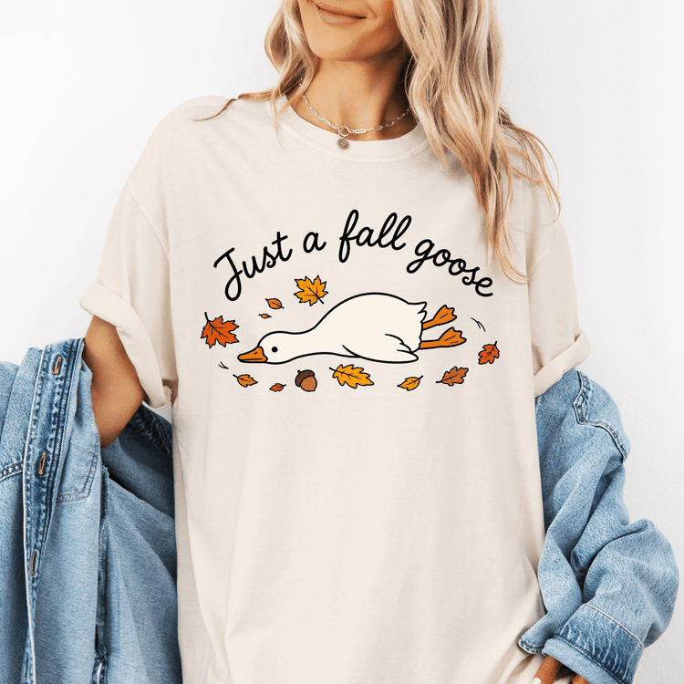 A woman wearing a white t-shirt with a graphic design of a goose surrounded by autumn leaves.
