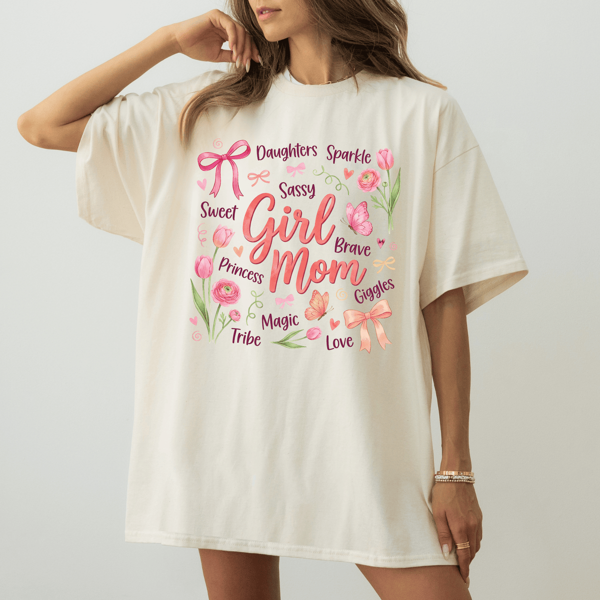 A woman wearing a white t-shirt with a printed design of various words and phrases related to a mother, including "Daughters", "Sparkle", "Sweet", "Sassy", "Girly", "Princess", "Goddles", "Magic", "Love", and "Tribe".