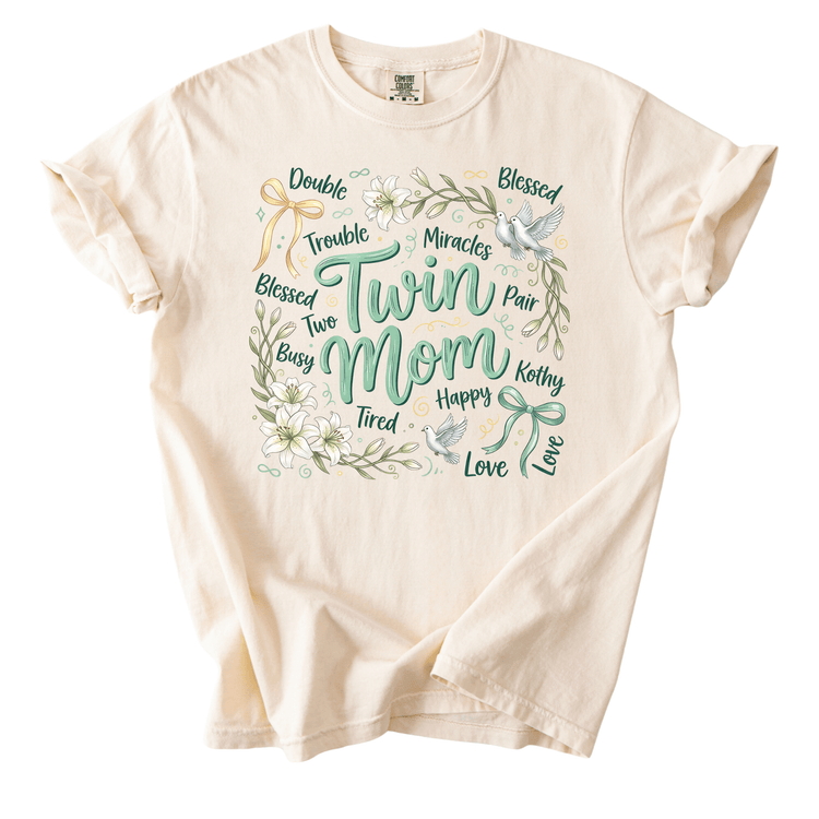 The image is a t-shirt with a graphic design featuring the words "Twin Mom" surrounded by various floral and bird-like elements.