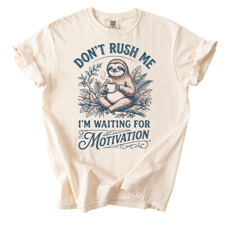 a t-shirt with a graphic design of a sloth holding a cup of coffee, accompanied by the text "Don't Rush Me I'm Waiting for Motivation".