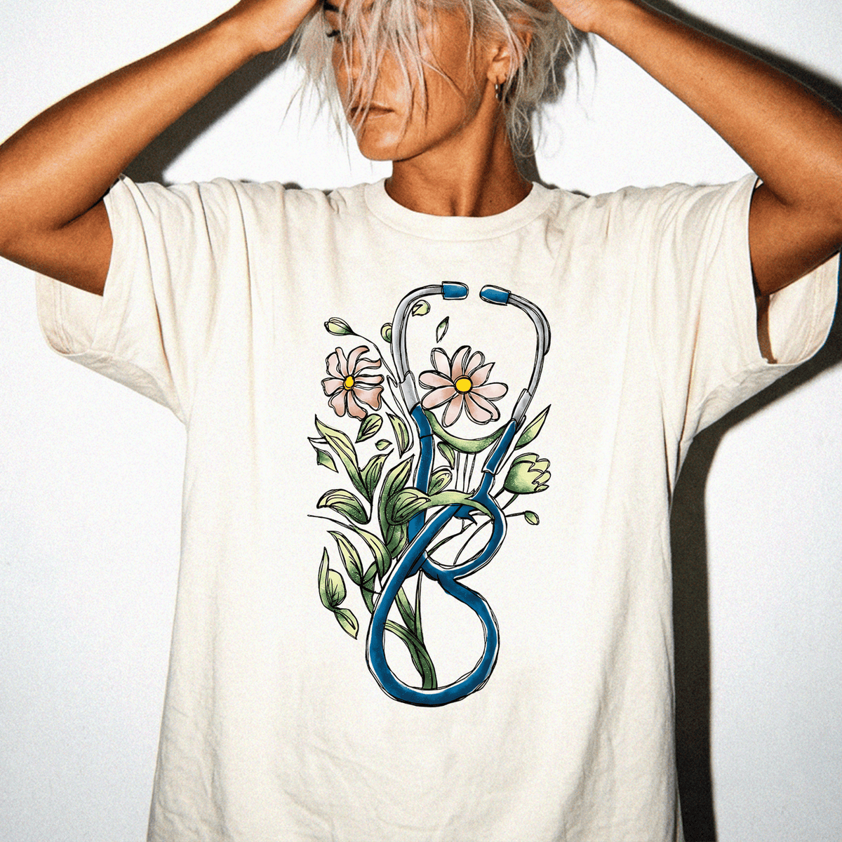A person wearing a white t-shirt with a graphic design of a stethoscope and flowers.