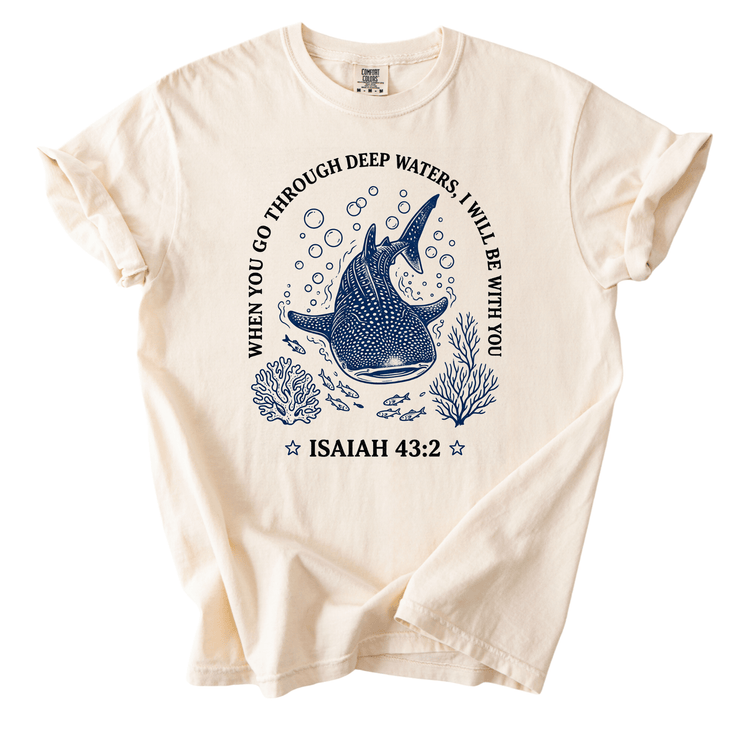 a white t-shirt with a graphic design depicting a blue whale surrounded by bubbles and marine life. The design includes text that reads "When you go through deep waters, I will be with you" and " Isaiah 43:2".