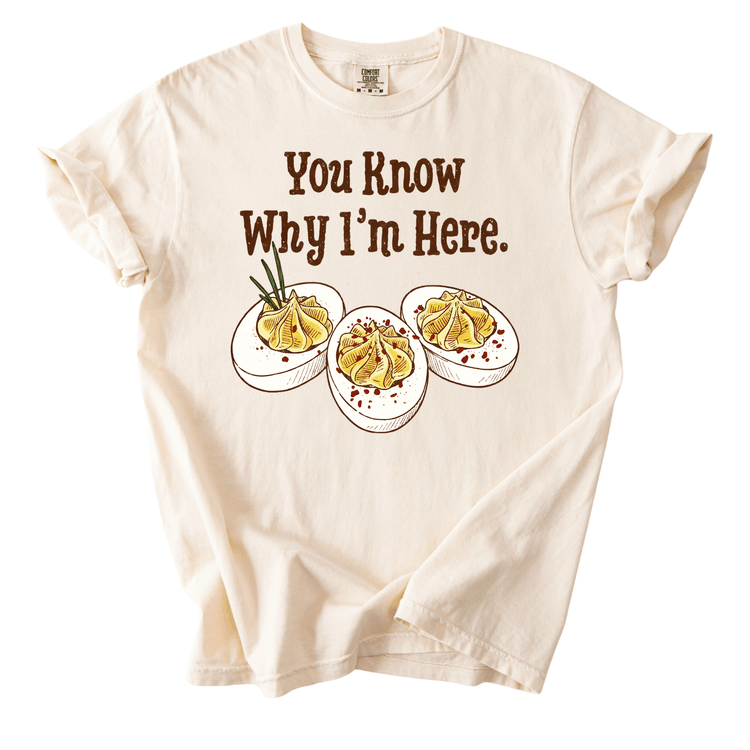 A white t-shirt with a graphic design featuring three deviled eggs with a humorous caption that reads "You Know Why I'm Here."