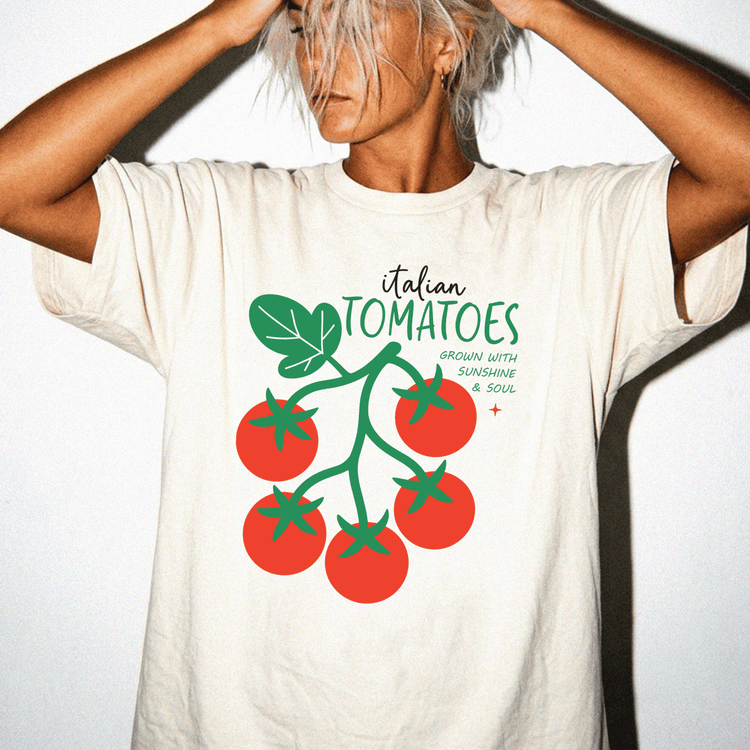 A person wearing a white t-shirt with a graphic design of tomatoes and the text "Italian TOMATOES GROWN WITH SUNSHINE & SOUL" printed on it.