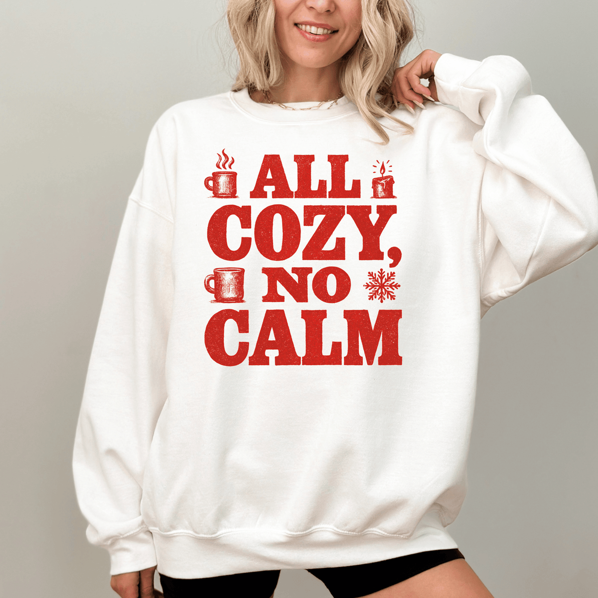 A woman wearing a white sweatshirt with a red text design that says "ALL COZY, NO CALM".