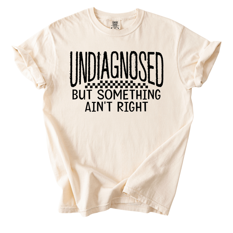 a white t-shirt with a bold, black text design that reads "UNDIAGNOSED BUT SOMETHING AIN'T RIGHT".